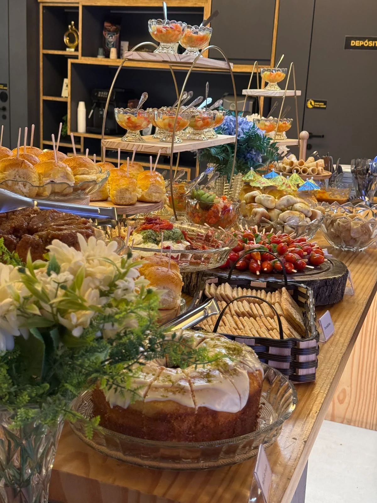 Mesa Áurea com bolos, mini sanduíches, frios, frutas e flores para coffee break corporativo